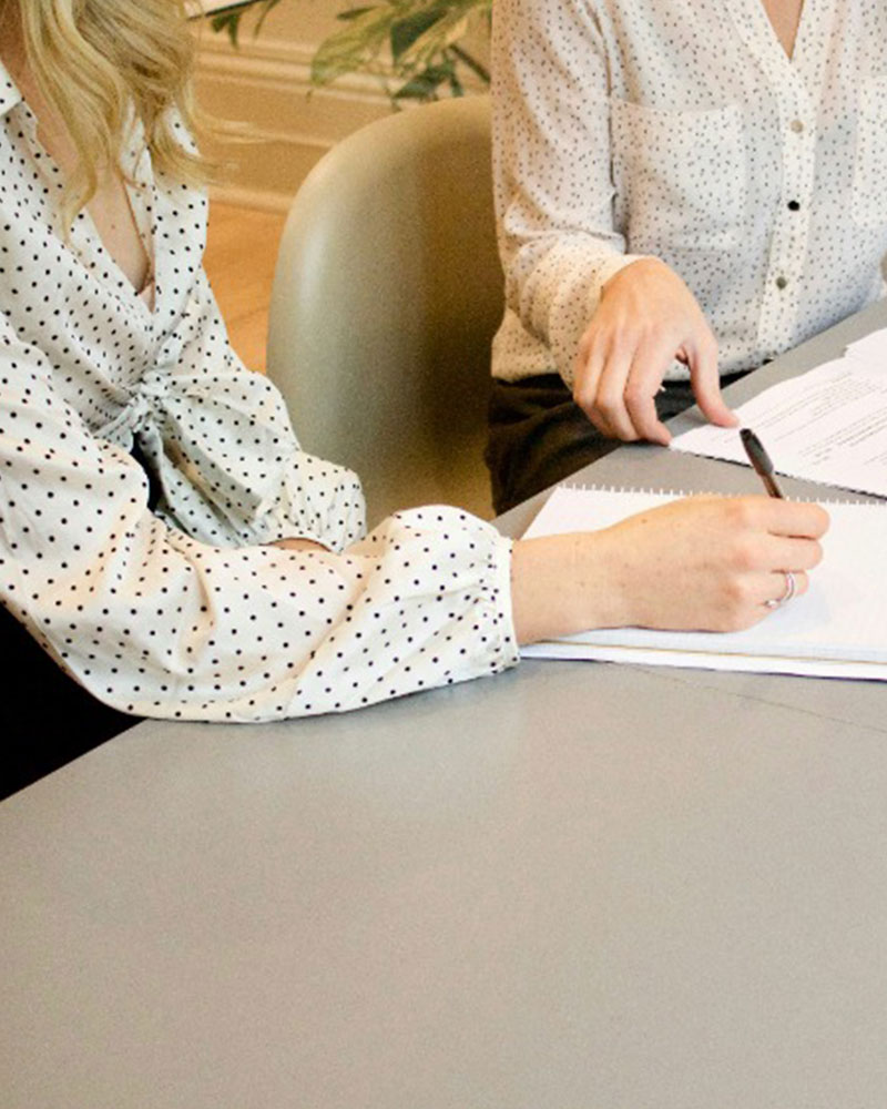 Two people in polka dot blouses sign documents at a table during a meeting.