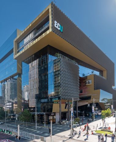 Corner of a modern glass office building with angled louvers against a clear blue sky (ECU logo visible).
